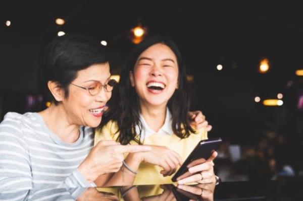 asian mother and daughter looking at a phone screen together, laughing in a cafe